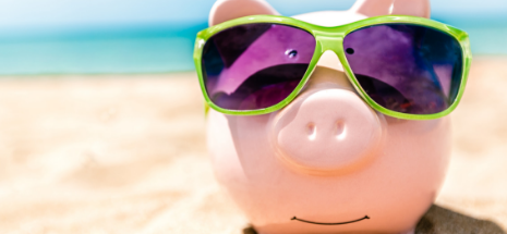 Photo of a piggy bank with sunglasses on the sand at the beach 